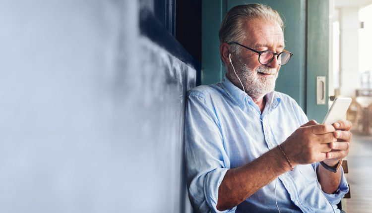 Happy male senior listening to songs on his cellphone