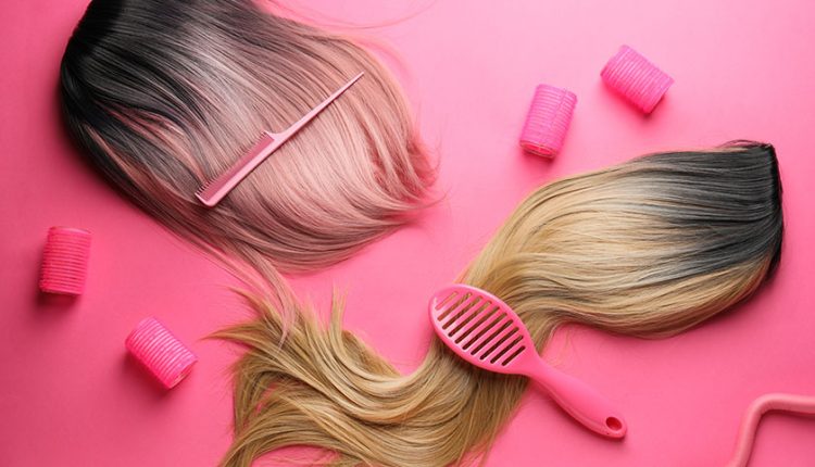 Female wigs, brush, comb and curlers on a pink background