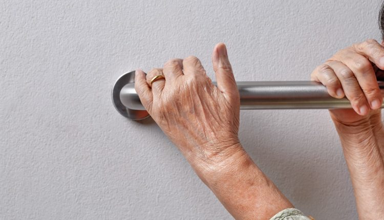 Hands of a senior on a grab bar installed on a wall which is a must for living alone elderly