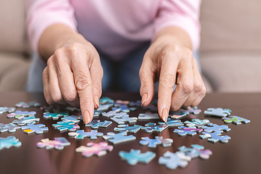 Senior woman hands doing jigsaw puzzle at home, panorama, close up