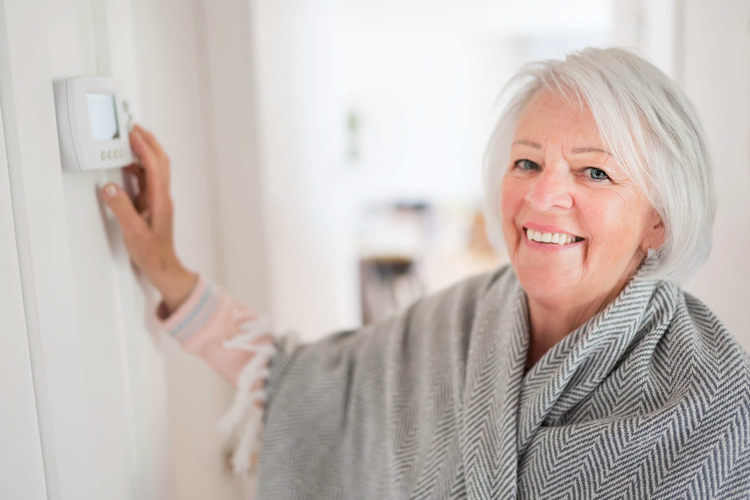 A,Senior,Woman,Adjusting,Her,Thermostat,At,Home