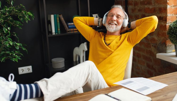 Happy and smiling senior man leaning back in his chair listening to his favorite playlist