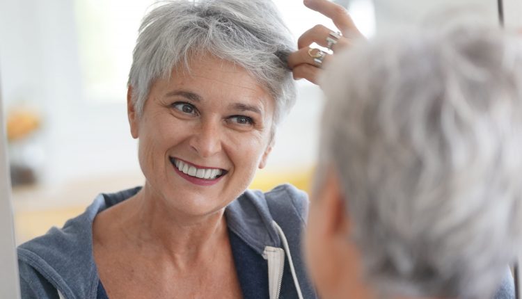 Attractive senior woman with short grey hair smiling and checking her hair in the mirror