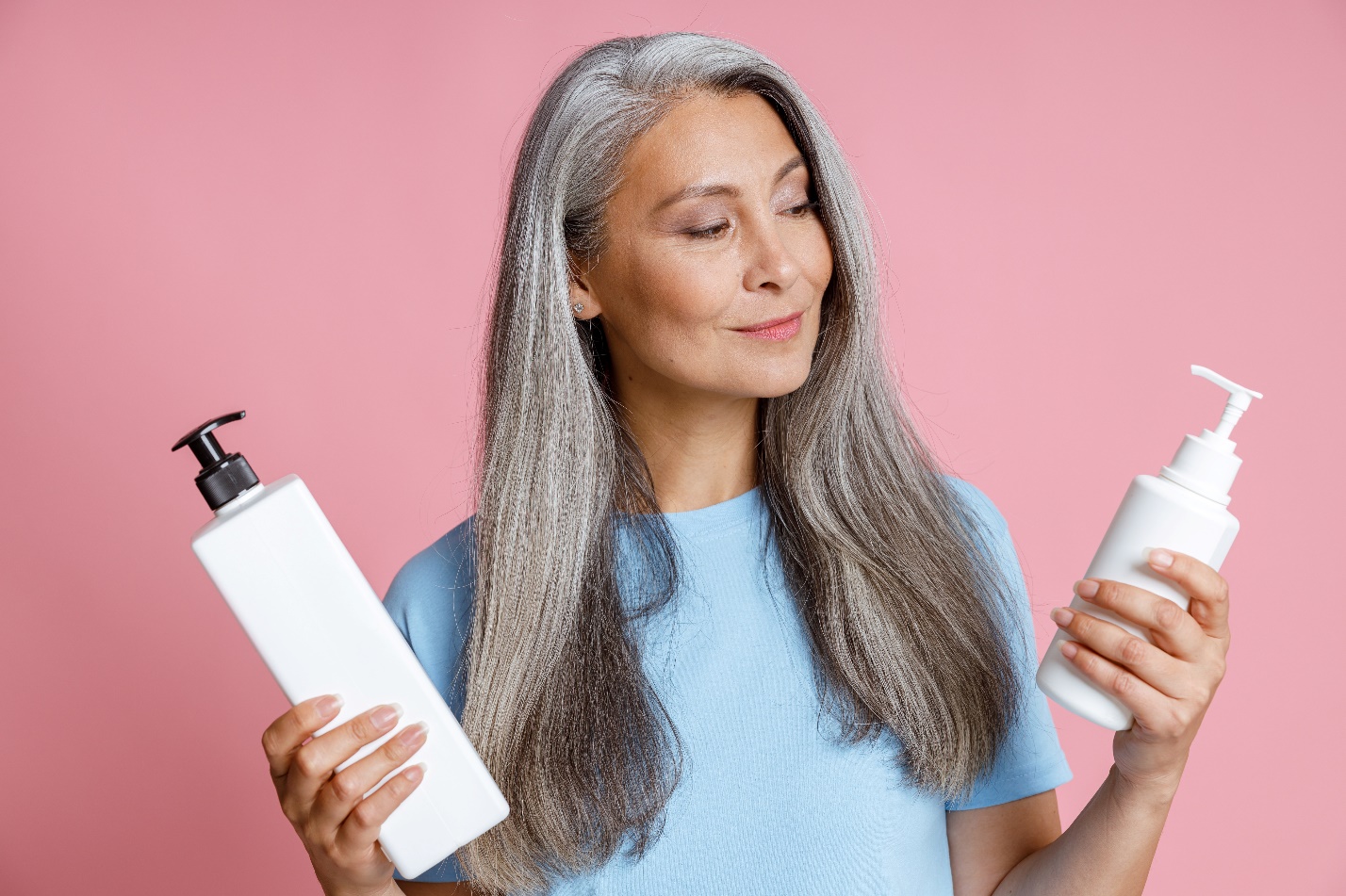 Senior woman with long grey hair holding two bottles of shampoos