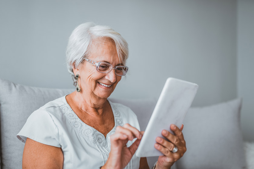 Senior woman smiling and reading books on her tablet