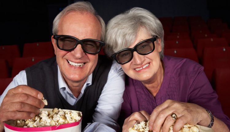 Happy senior couple in a movie theater wearing glasses and eating popcorn