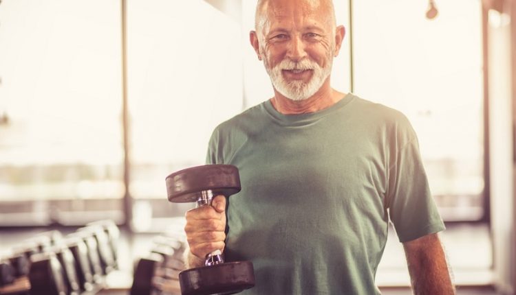 Smiling senior man with weight at gym. Looking at camera.