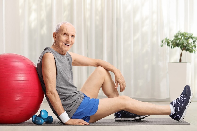 Elderly man with fitness ball and dumbbells sitting on an exercise mat at home