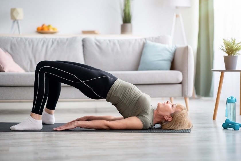 Strong mature woman doing half bridge yoga pose, strengthening her abs muscles.