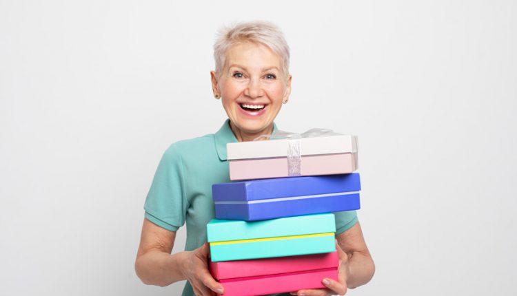 Happy senior woman holding up four gift boxes in different colours