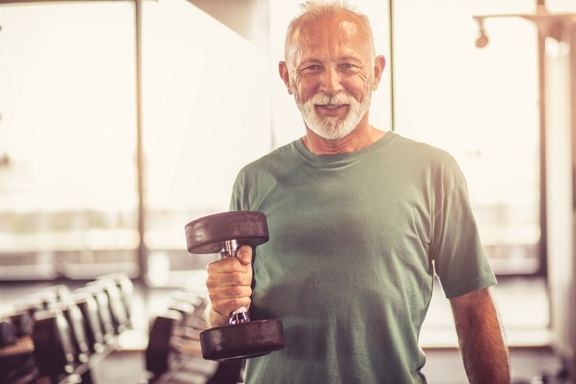 Smiling senior man with weight at gym. Looking at camera.