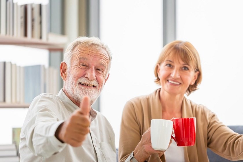 Senior couple inside home during a coffee break, Smiling elderly couple showing thumbs up with holding cups of coffee