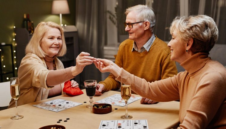 A group of seniors, two women and one man, sitting at the table with snacks and drinks at a retirement party and playing a board game