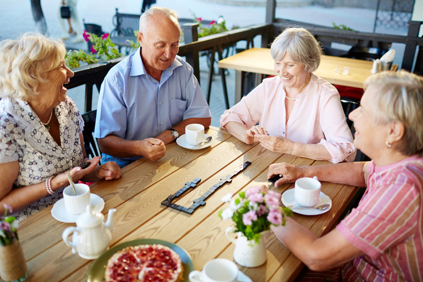 A group of seniors sitting a table and smiling while playing dominoes