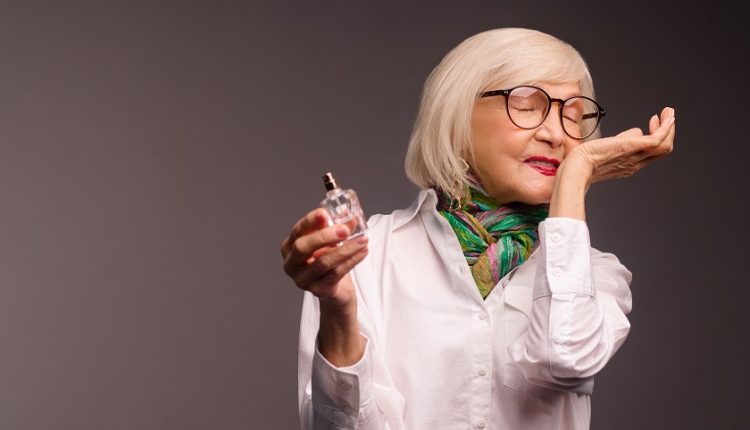 An older woman's wrist is scented with perfume, and she smells it