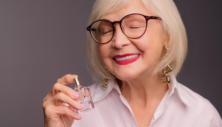 An older woman's smelling a perfume.