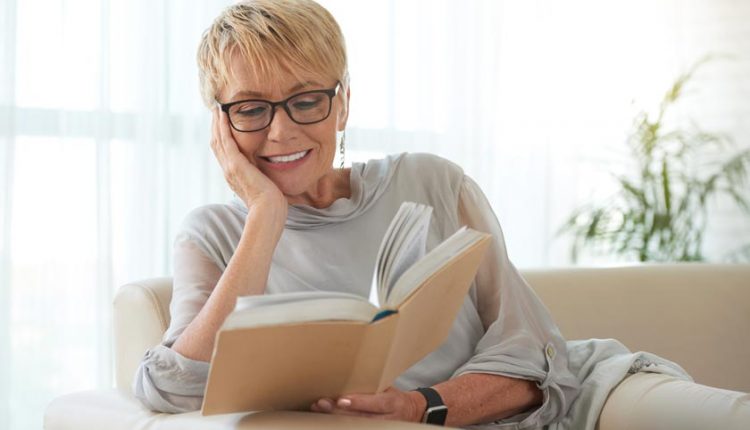 Attractive senior woman with glasses reading a book and smiling