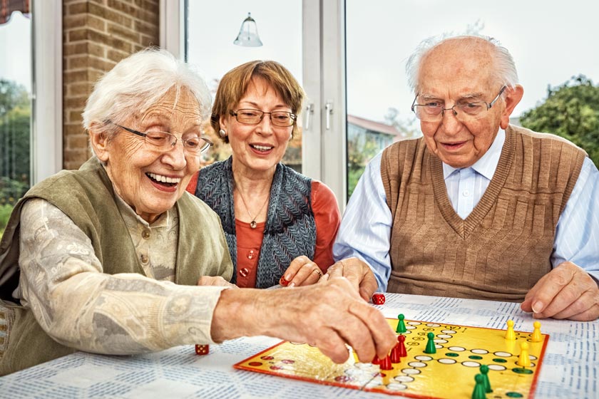 games to play with dementia patients, games to play with the elderly with dementia, Three seniors, one male, two females, playing a board game happily