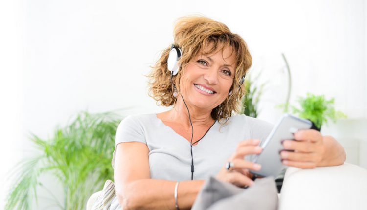 Senior woman smiling while holding her mobile phone and wearing headphones