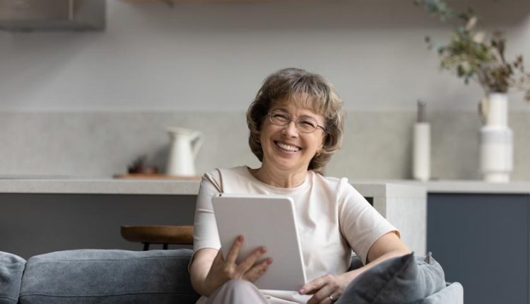 Happy senior woman sitting on a couch and playing with her tablet