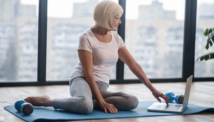 Senior woman sitting on a yoga mat on an online yoga class with her laptop