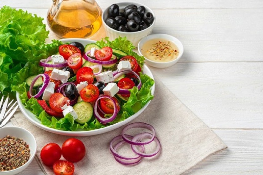 Greek salad and fresh ingredients on a white wooden background. Side view with copy space.