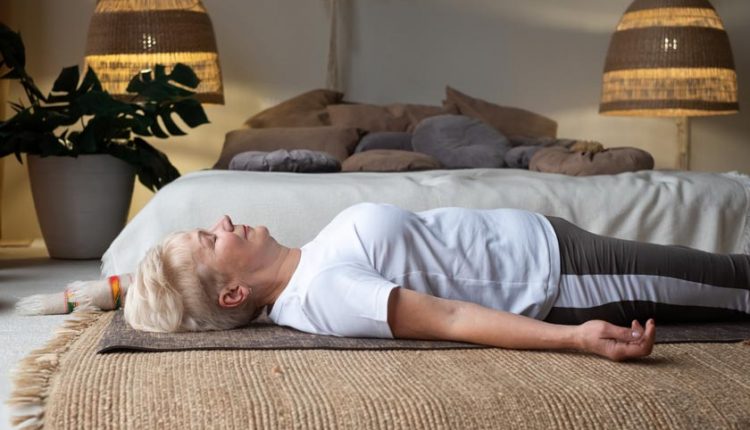 Senior woman doing a yoga pose in front of her bed