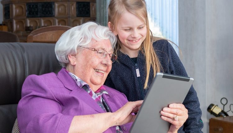 A senior's holding an iPad as she stands with her grandchild 
