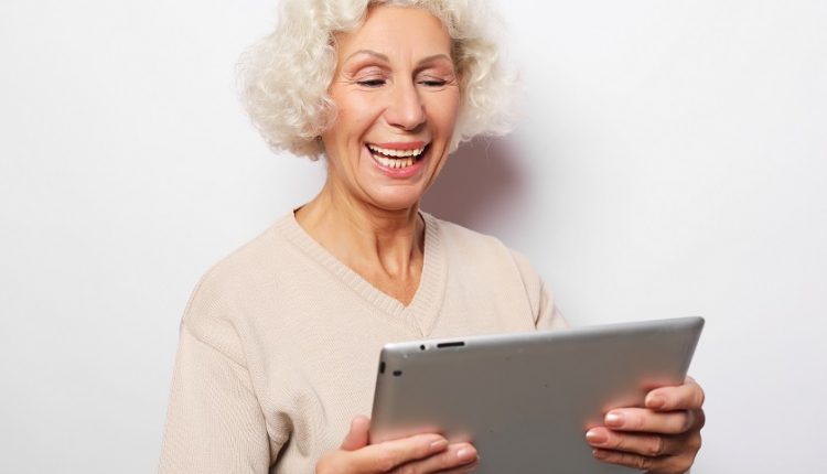 Female senior smiling while holding an iPad 