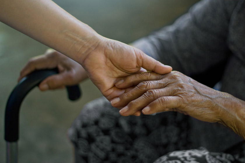 View of a senior's hands holding the hand of another person and communicating