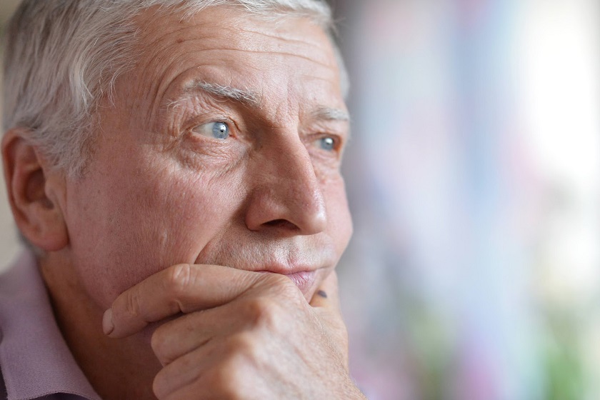Old man, placing his hand under his chin, looking outside.