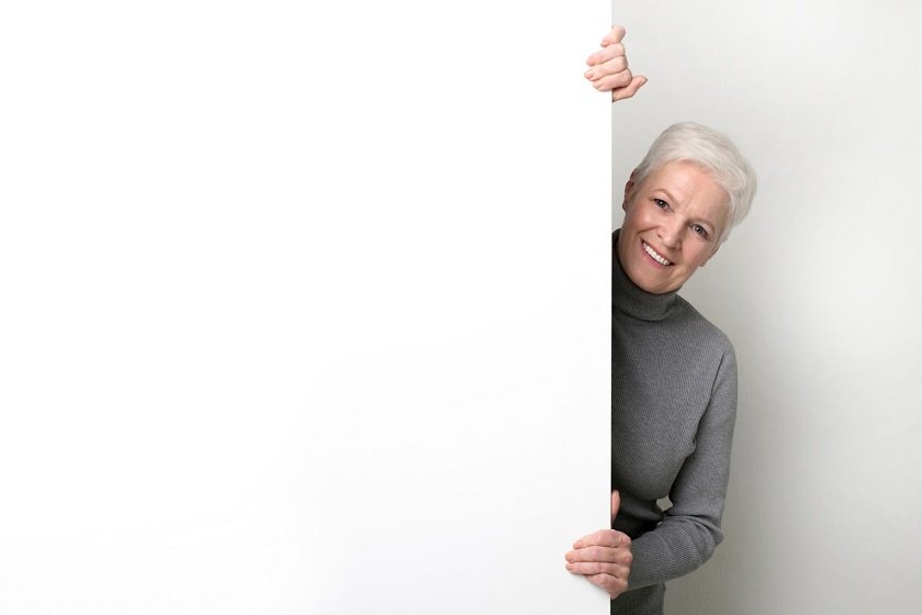 Senior woman smiling, standing behind a white board