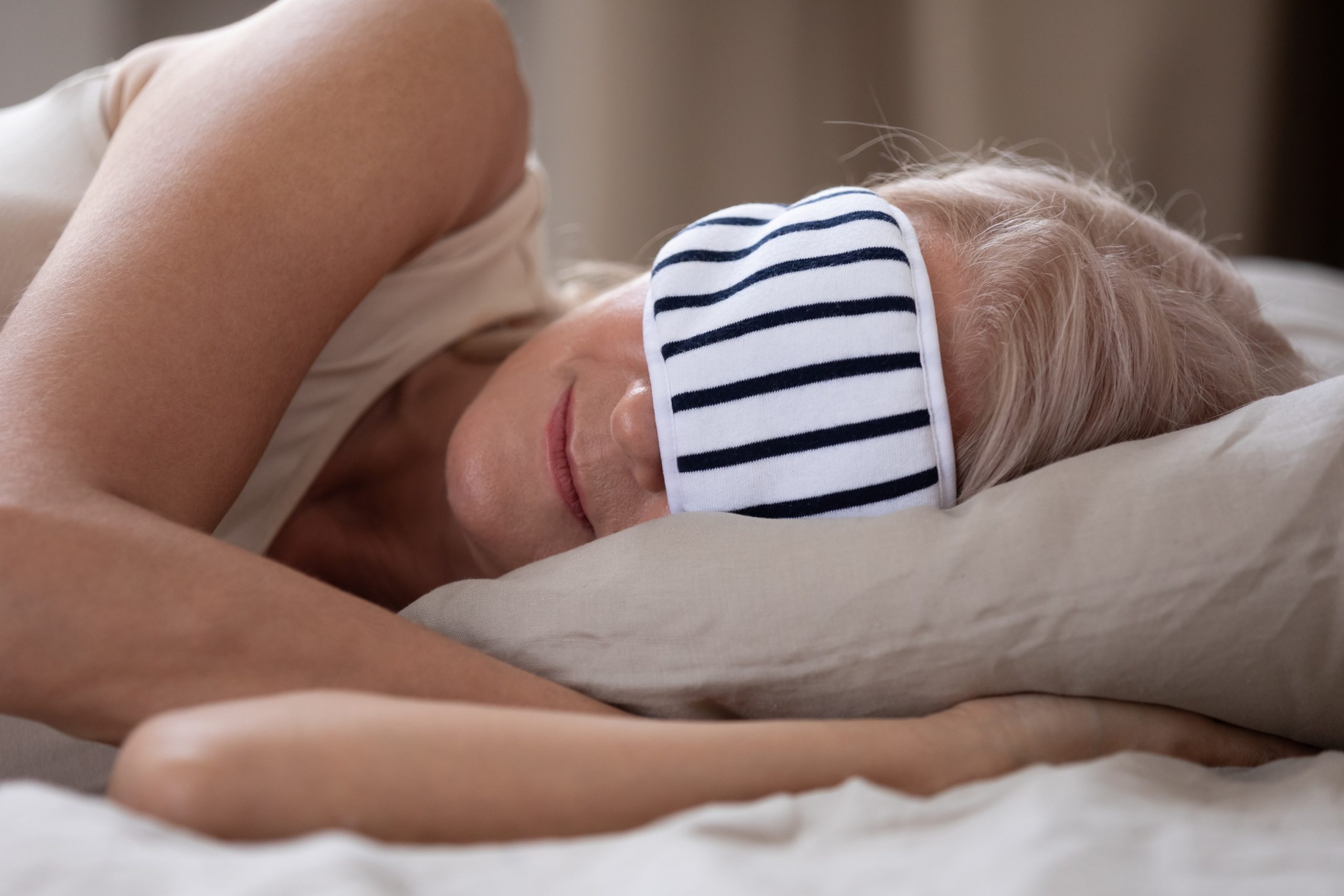 Naps and Alzheimer's. Calm mature woman wearing striped sleeping mask relaxing in comfortable bed