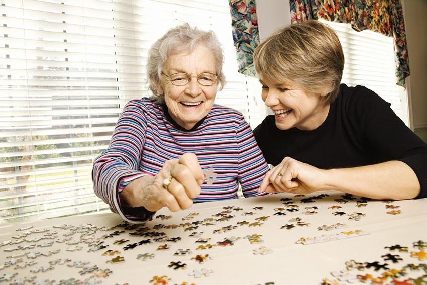 puzzles for alzheimer's patients: senior woman and a middle-aged woman happily solving a jigsaw puzzle together. 