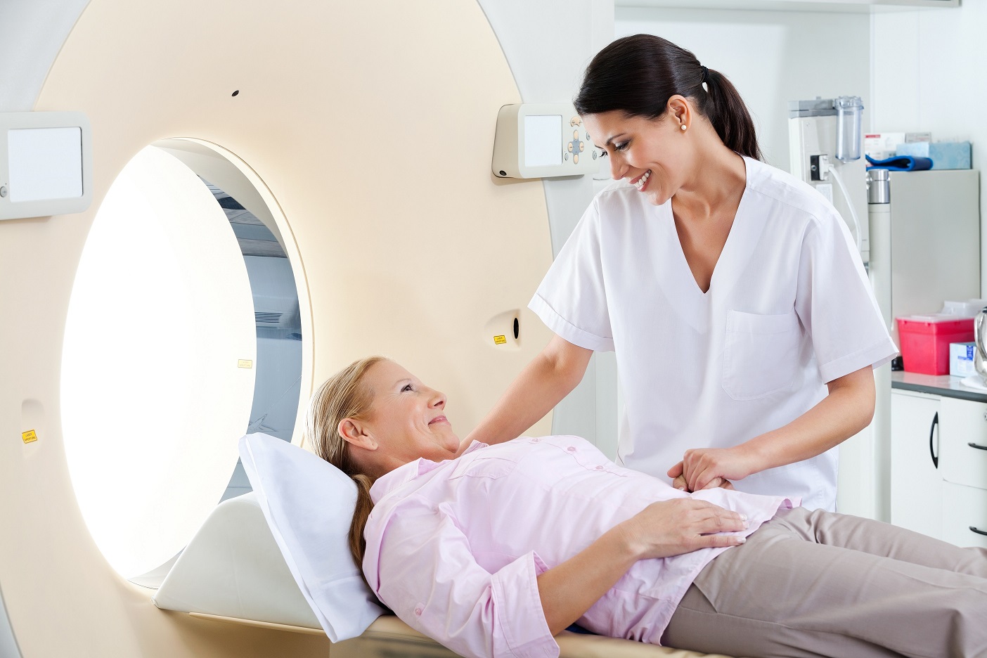 Radiologic technician smiling at mature female patient lying on a CT Scan bed, MRI and Alzheimer's