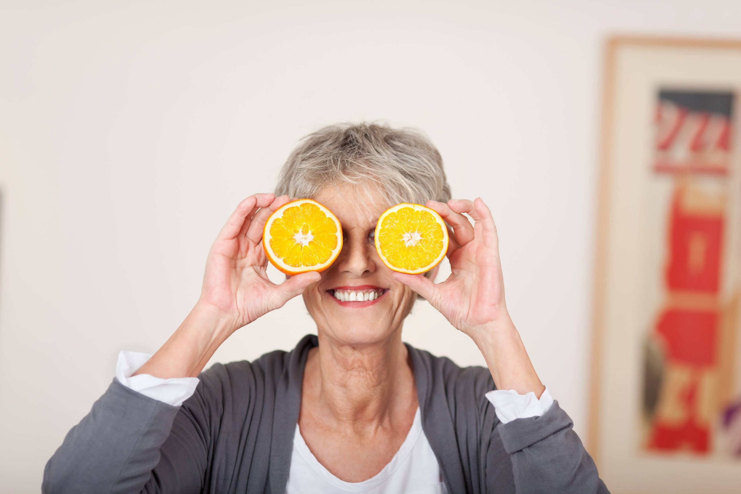 Senior woman smiling with orange in front of her eyes